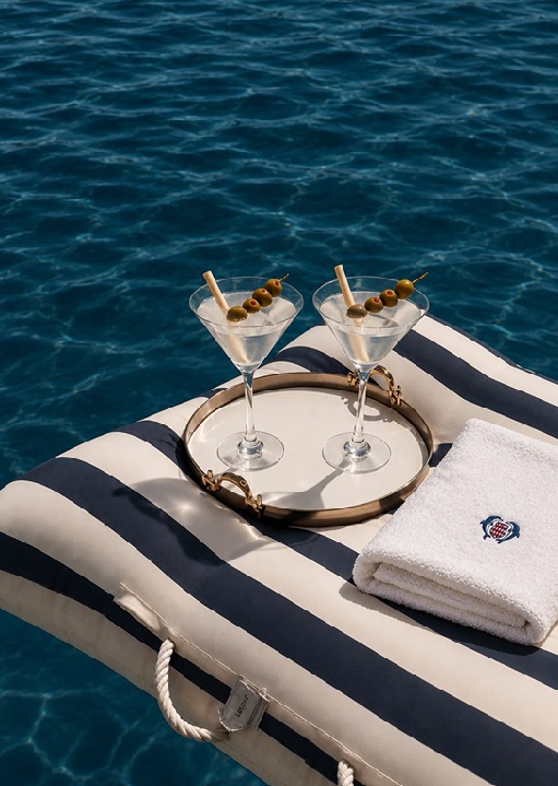 Two martinis and a folded towel on a striped float on the water